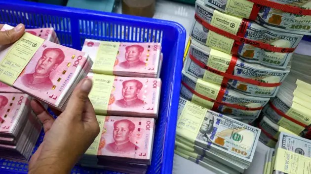 Một nhân viên ngân hàng tại Kasikornbank (Thái Lan) đang đếm tiền nhân dân tệ, đặt cạnh những tờ USD